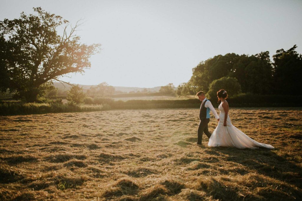 bride and groom walking across the meadow