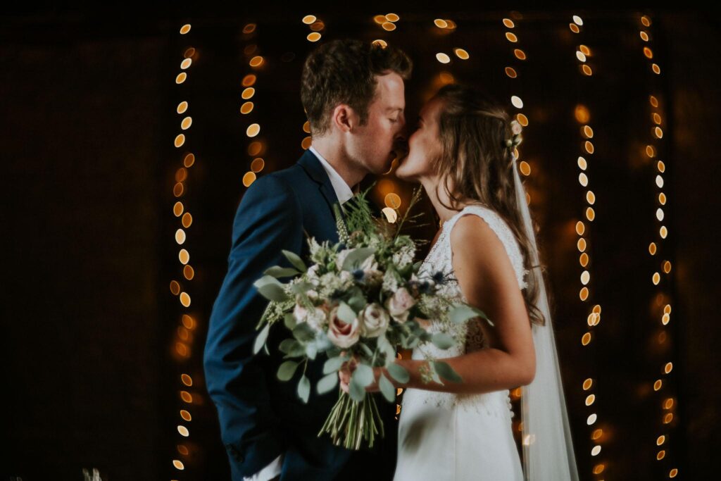 bride and groom kissing with the fairy lights in the garden