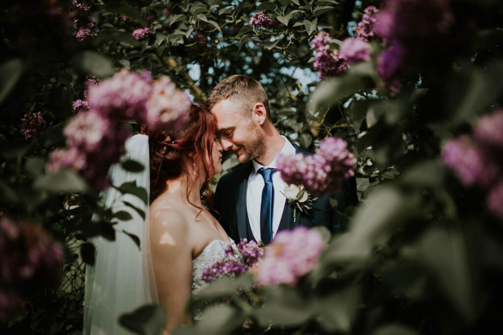 bride and groom kissing surrounded by the blooming lilac bush