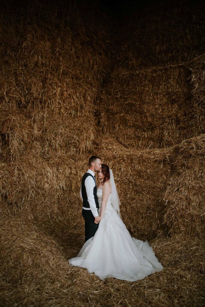 bride and groom surrounded by the large hay balls taken in the manor farm barn