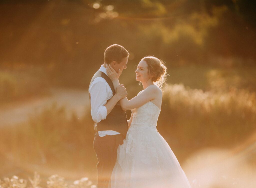bride and groom softly look at each other the sun is setting behind them creating a big orange flare on the photograph