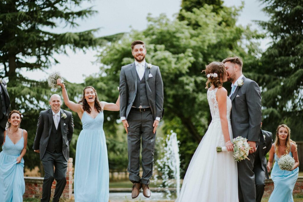 a funny group portrait of bride and groom kissing and wedding party members jumping
