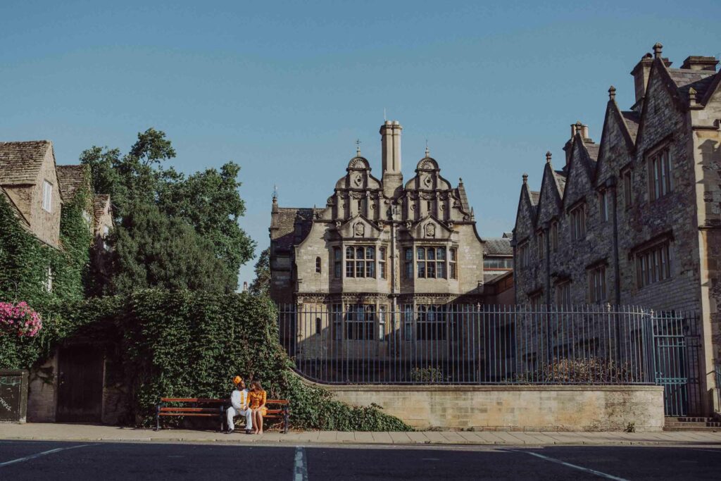 On a sunny day a couple sitting on the bench in front of Trinity College in Oxford