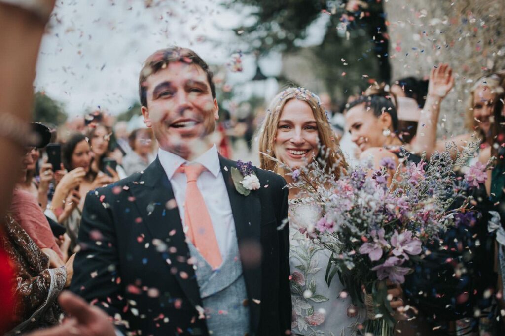 bride and groom passing by the confetti line. Lots of colourful petals flying in the air