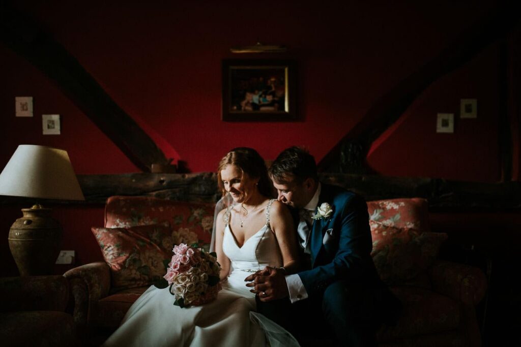 bride and groom siting on the couch. He is gently kissing her shoulder