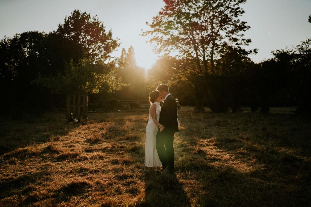bride and groom hugging on the meadow. The sun is setting on the horizon behind them