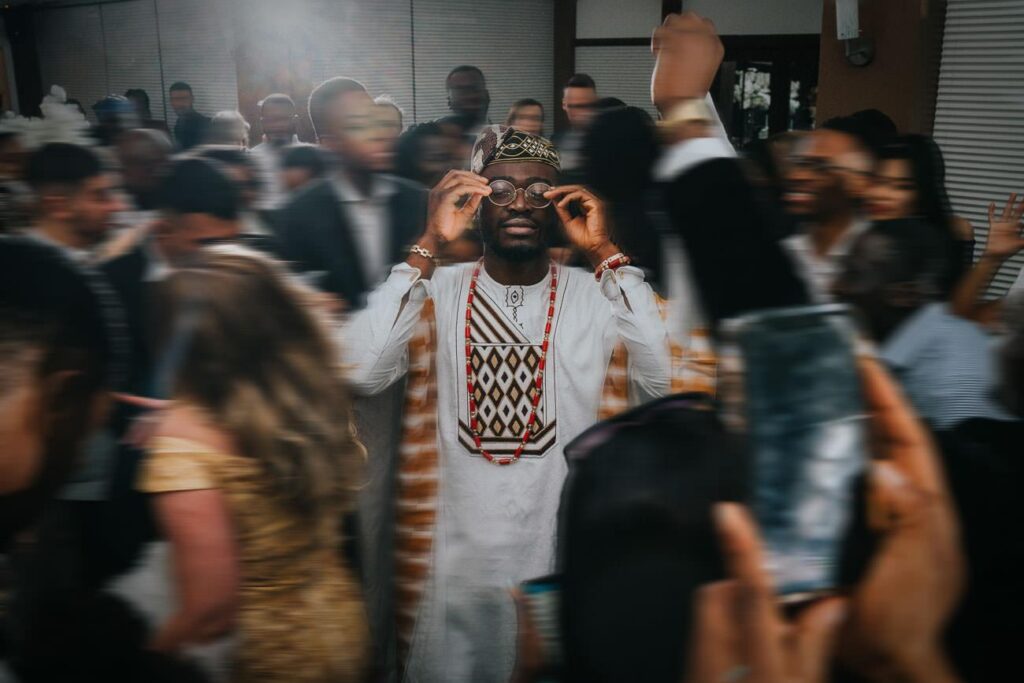 groom who is wearing traditional Nigerian outfit is standing in the middle of the dance floor, his guests are dancing around him
