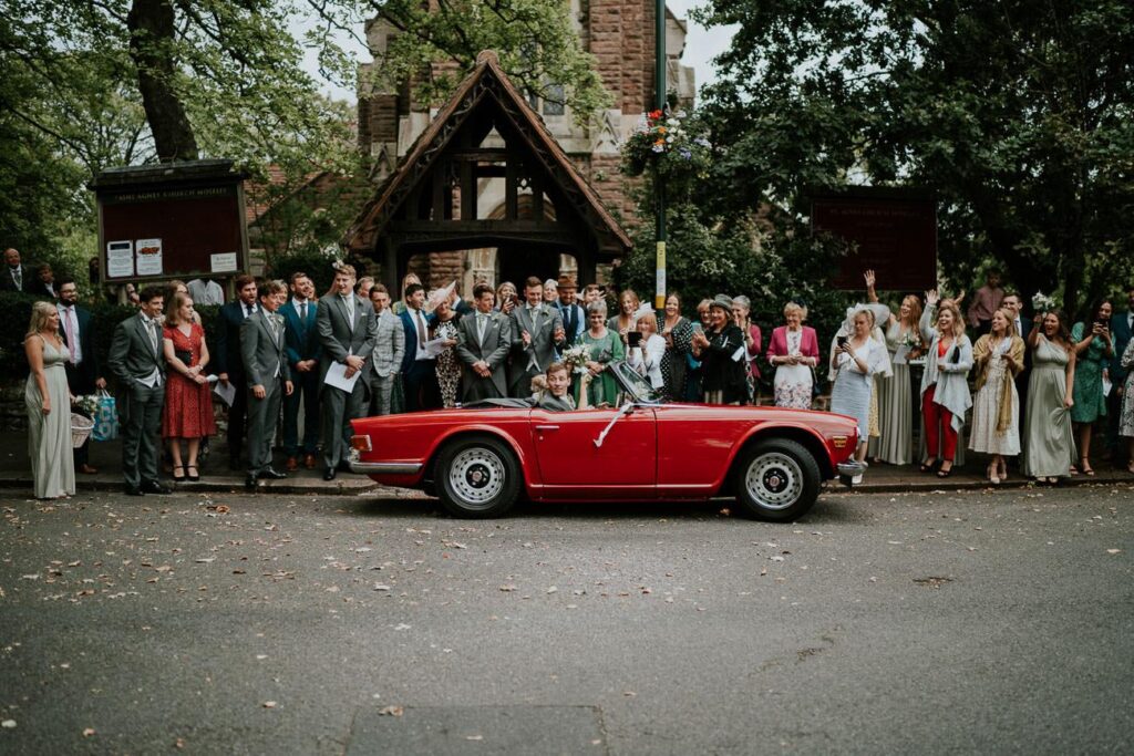 bride and groom leaving the church in the red cabriolet