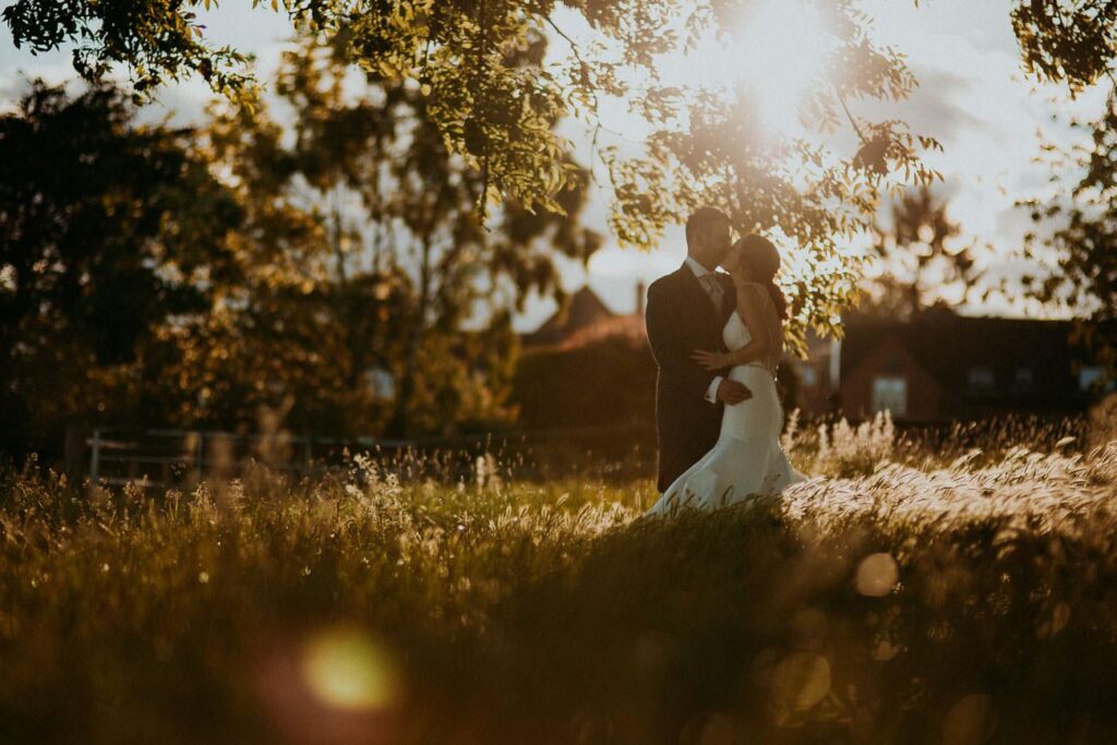 bride and groom kissing in the garden. The are standing in the tall grass that is being gently moved by the wind