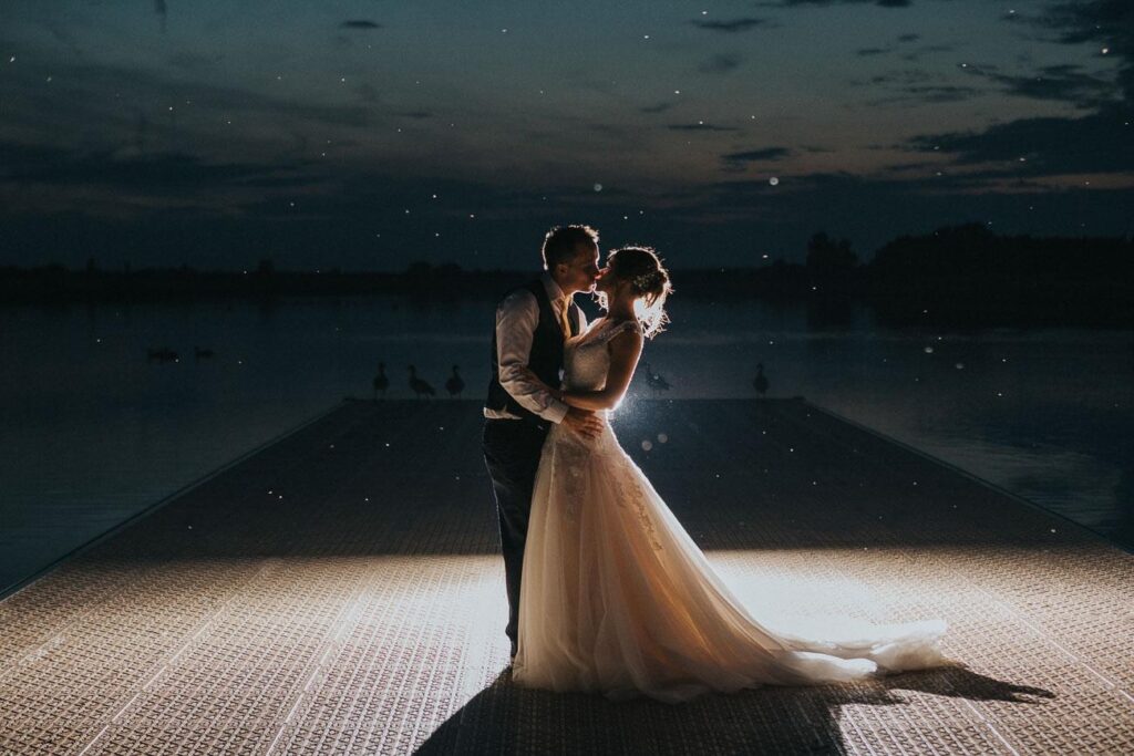 image of the bride and groom standing on the bridge by the lake surrounded by the flock of geese