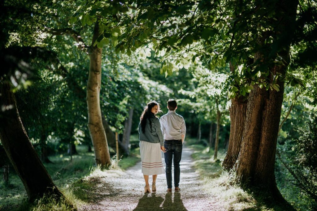 smartly dressed engaged couple is taking a walk in the Magdalen College gardens. she is looking over the the shoulder at the camera