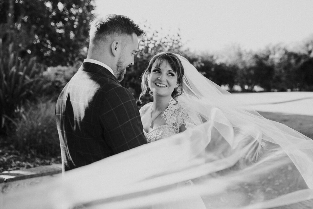 black and white image of bride and groom. wind is plying with the brides veil