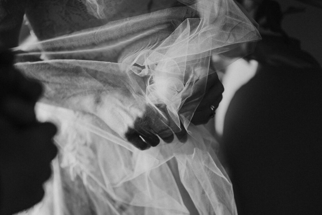 black and white image of bride holding her vail that is being blown by the wind