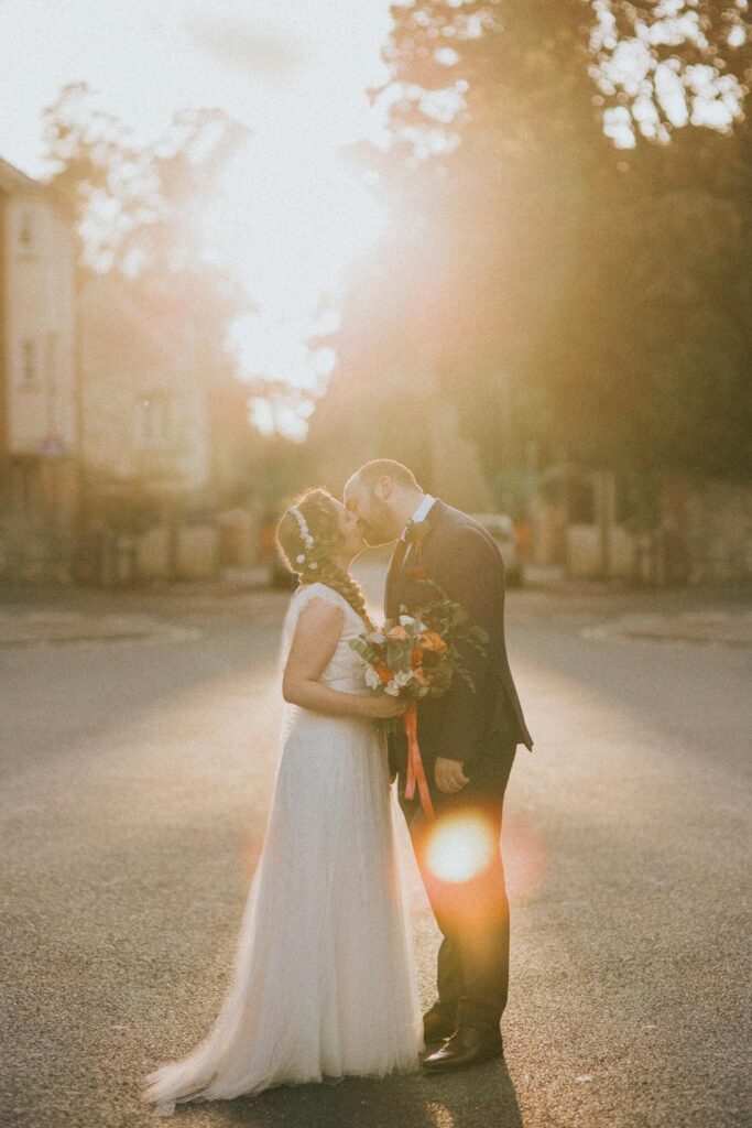 bride and groom kissing whilst standing on the road in oxford town centre. the sun is setting in the background