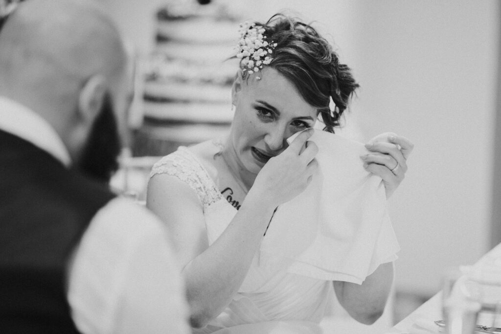 black and white image of emotional bride wiping her eyes with a hand