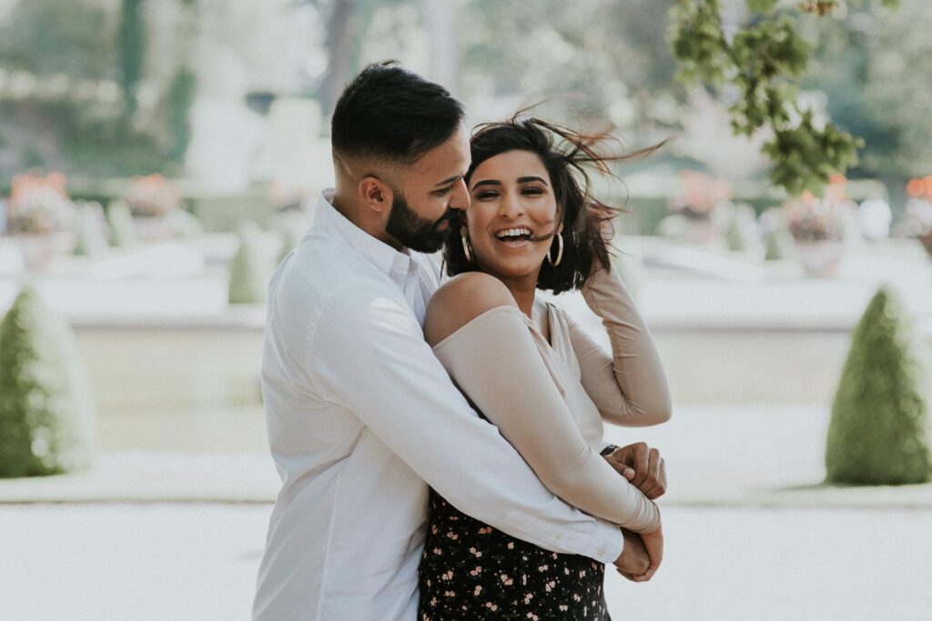 newly engaged couple hugging in the Blenheim palace gardens. She is joyfully laughing, the wind is plying with her hair