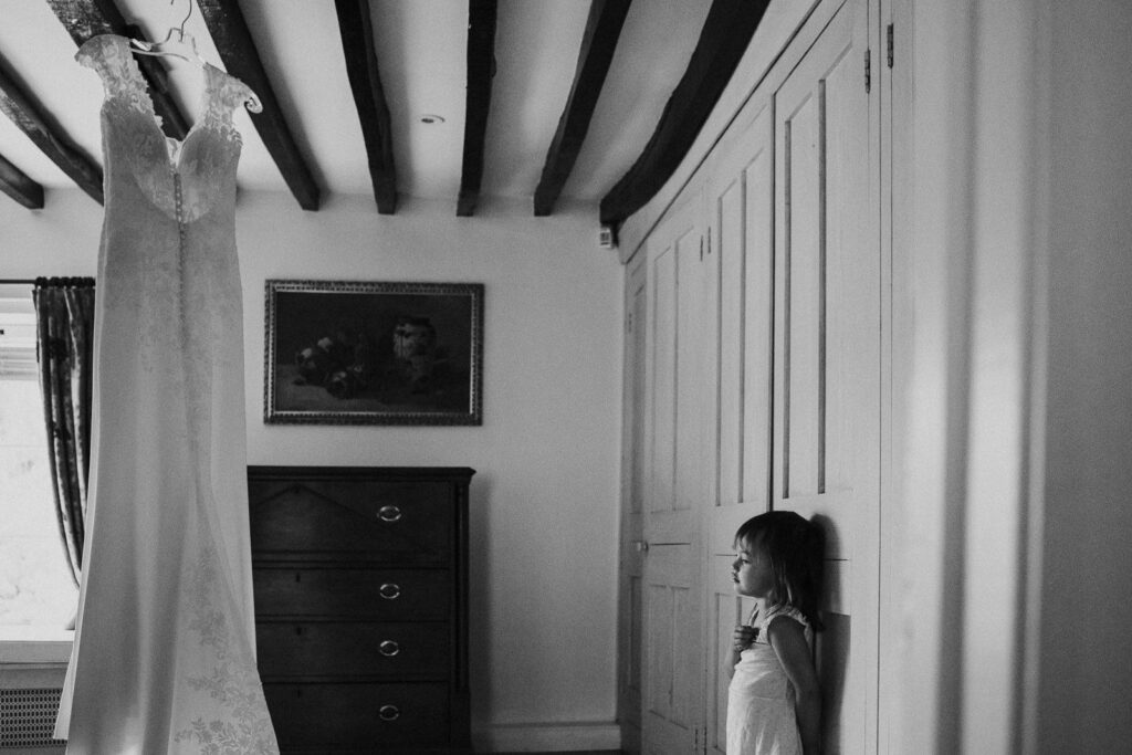 black and white image of a little girl deep in thought looking on the wedding dress