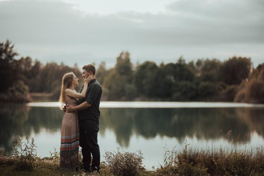 engagement image of man and women in a maxi dress, facing each other with the lake in the backdrop
