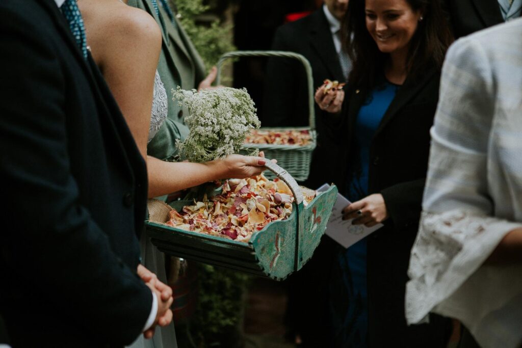brides maid is holding green wooden basket filled with the confetti