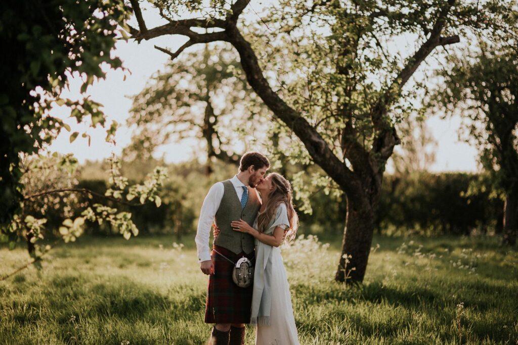 bride and groom kissing in the apple orchard filled with a sunset light