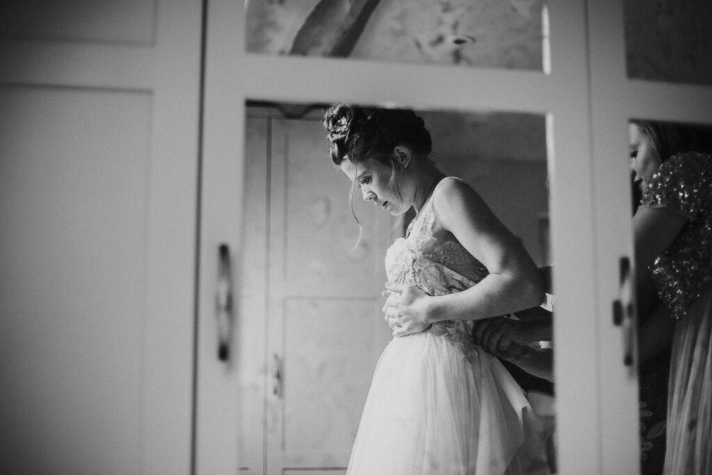 black and white photograph of bride to be being helped to put her dress on